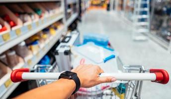 Human Hand Close Up With Shopping Cart in a Supermarket Walking Trough the Aisle photo