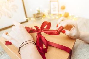 Woman wrapping present in paper with red ribbon. photo