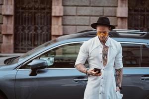 un joven con sombrero y gafas de sol sostiene un teléfono móvil en sus manos foto