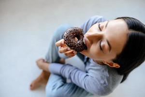 Portrait of rejoicing woman eats tasty donut at home. photo