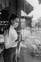 Young woman in face mask standing in front of windows in cafe. photo