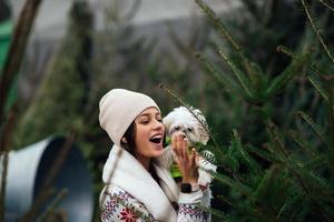 Woman with a white dog in her arms near a green Christmas trees photo