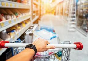 Human Hand Close Up With Shopping Cart in a Supermarket Walking Trough the Aisle photo