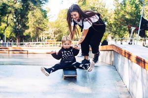 Young mother teaches her little boy to ride a skateboard photo