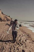 Man carries his girlfriend on back, couple having fun on the seashore photo