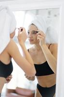 Woman in lingerie and a head towel applies makeup photo