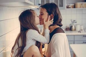 mamá besa a su pequeña hija en la cocina foto