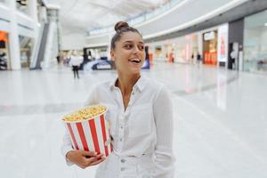 linda mujer joven sosteniendo palomitas de maíz en el fondo del centro comercial foto