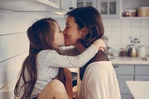 Mom kisses her little daughter in the kitchen photo