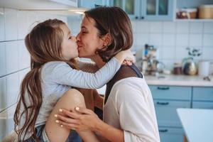 Mom kisses her little daughter in the kitchen photo