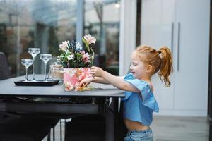 Little girl puts flowers on table photo