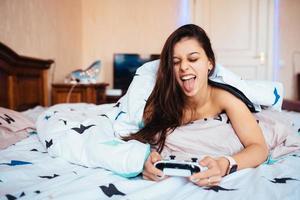 chica divertida acostada en la cama y jugando videojuegos, sosteniendo el controlador foto