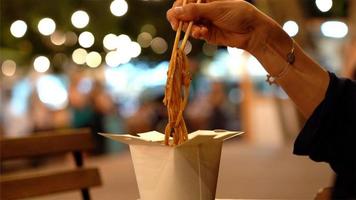 Cardboard box of asian food and hand holding chopsticks. photo