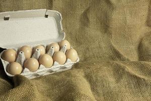 caja de papel con huevos de gallina frescos de granja sobre fondo de tela de saco foto