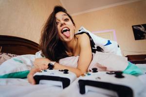 chica divertida acostada en la cama y jugando videojuegos, sosteniendo el controlador foto