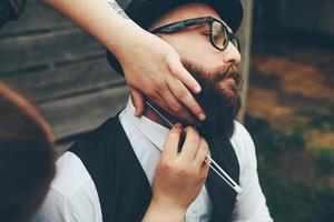 peluquero afeita a un hombre barbudo al aire libre foto