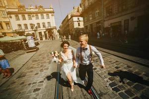 the bride and groom running along streets photo