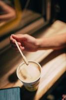 A female hand holding a stick over a latte paper mug photo