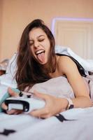 Funny girl lying in bed and playing video game, holding controller photo