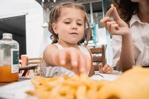 Mom and daughter eat french fries at an outdoor cafe photo