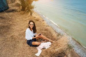 attractive woman in summer skirt and shirt sits on the shore photo