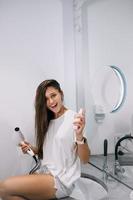 Young beautiful woman in the bathroom holding a hairdryer and a small bottle photo