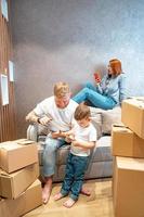 Young happy family with kid unpacking boxes together sitting on sofa photo