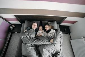 niño feliz con los padres en la cama en casa foto