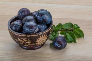 Fresh plums in a bowl on wooden background photo