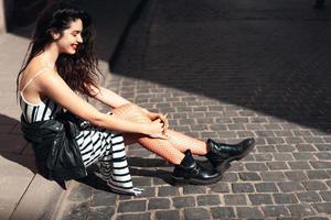 Beautiful fashionable lady sitting on old street photo