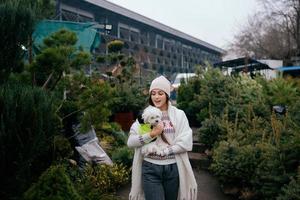 Woman with a white dog in her arms near a green Christmas trees photo