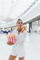 linda mujer joven sosteniendo palomitas de maíz en el fondo del centro comercial foto