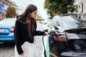 mujer cerca de coche eléctrico. vehículo cargado en la estación de carga. foto