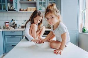 Two little girls in the kitchen sitting on the table. photo