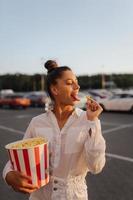 linda mujer joven sosteniendo palomitas de maíz en el estacionamiento de un centro comercial foto