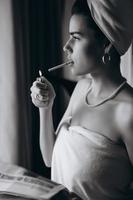 hermosa joven en una toalla fuma un cigarrillo y lee el periódico
