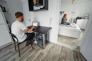 Dad works at laptop, mom and baby on the bed photo