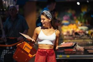 mujer joven elige carne en una tienda de comestibles foto