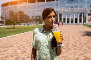 mujer joven sonriendo y bebiendo un cóctel con hielo en un vaso de plástico con paja foto