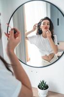 Young woman applying lipstick looking at mirror photo