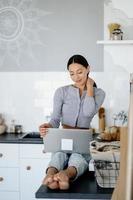 imagen de una linda morena sentada en la cocina y usando una laptop foto