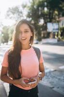 hermosa mujer morena con mochila y teléfono móvil en la calle foto