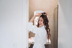 Beautiful smiling woman curling long hair using curling iron. photo