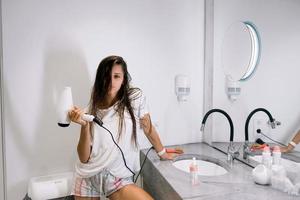 Young beautiful woman in the bathroom holding a hairdryer photo