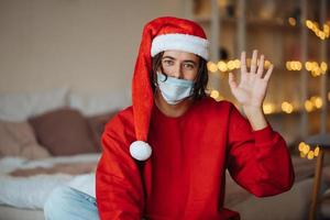 Caucasian guy in face mask and Santa Claus hat looking at camera photo