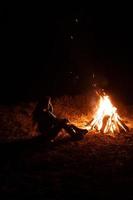 Woman sitting and getting warm near the bonfire in the night forest. photo