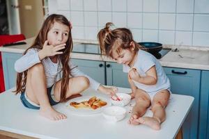 Two little girls in the kitchen sitting on the table. photo