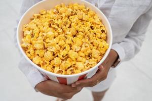 Close-up photo of a young sweet girl, who is holding a tube of popcorn in her hands.