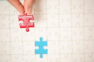 Close up hand holding and playing jigsaw game incomplete. White part of jigsaw puzzle pieces on blue background. concepts of problem solving, business, teamwork. photo