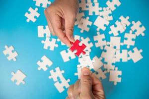 Close up hand holding and playing jigsaw game incomplete. White part of jigsaw puzzle pieces on blue background. concepts of problem solving, business, teamwork. photo